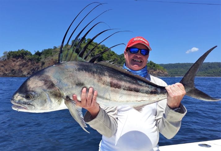 angler with red hat holding a roosterfish for photo
