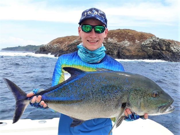 Junior angler posing with Bluefin Trevally Waves breaking on rocks in background