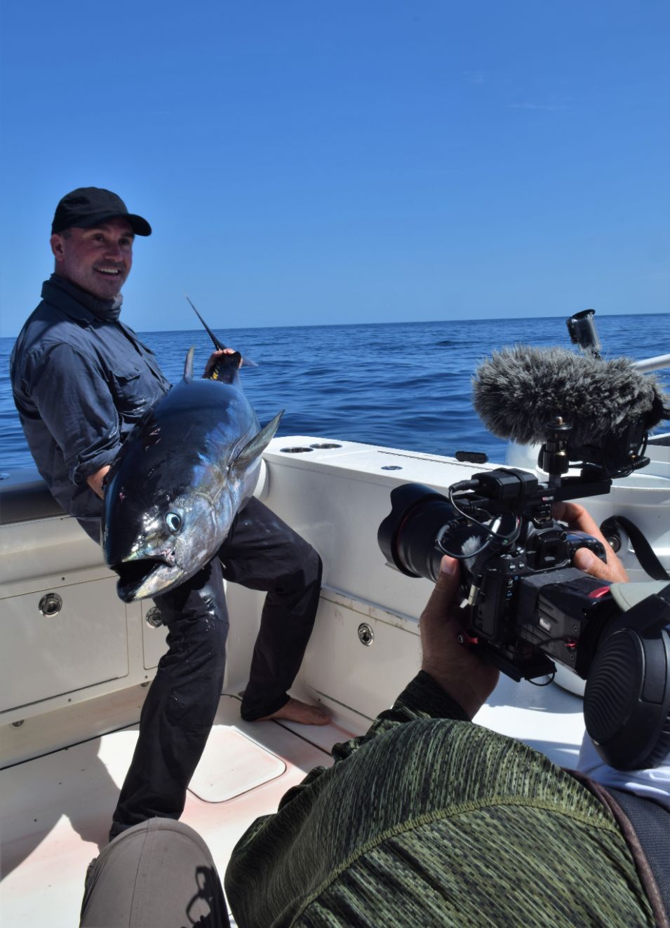 Angler holding yellowfin tuna with camera man in foreground
