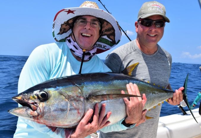 Two smiling anglers holding small yellowfin tuna