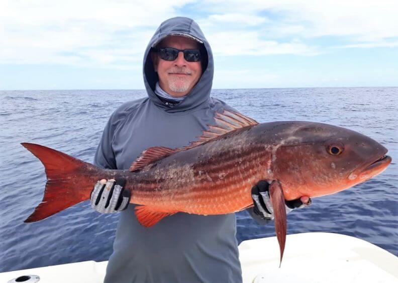 Angler in rain gear posing with mullet snapper.