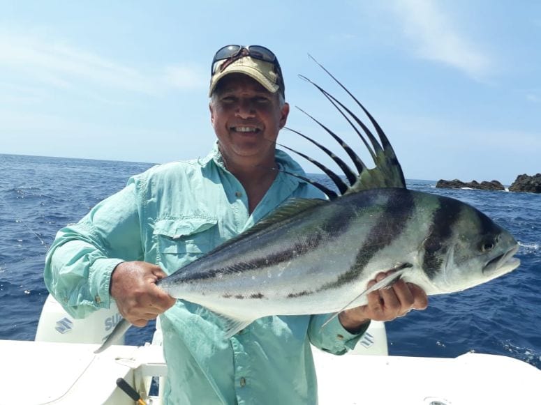 Angler posing with small roosterfish and rocks in background